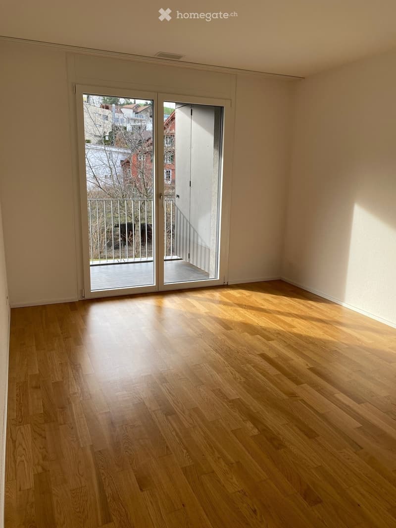 Empty room with light wooden flooring and large sliding glass doors leading to a balcony.