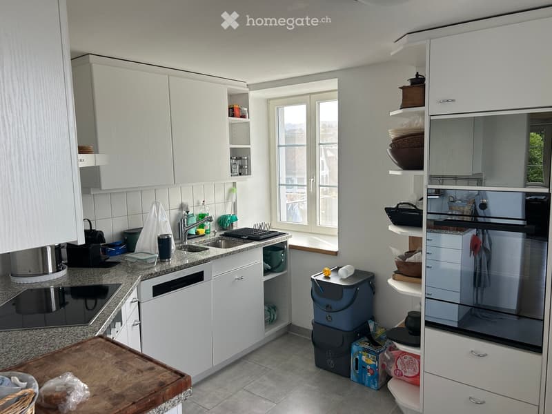 Modern kitchen with white cabinets, granite countertops, sink, oven, dishwasher, and various kitchen items.