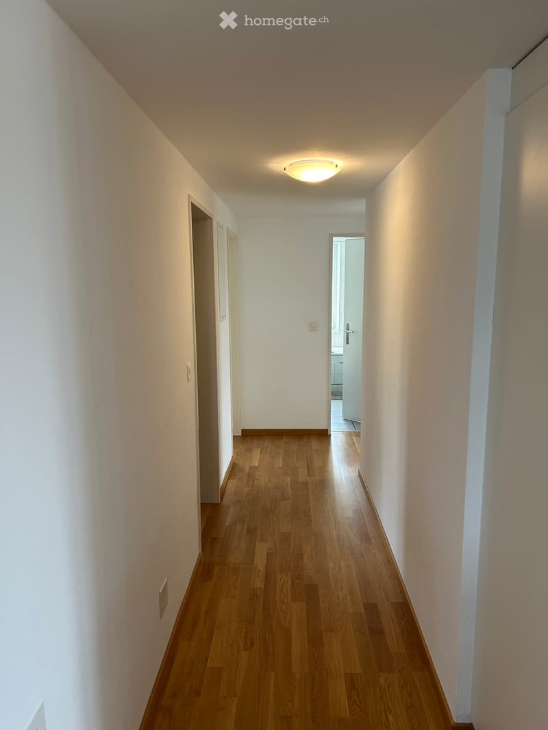 Empty hallway with wooden flooring, white walls, and recessed lighting. Doors lead to adjacent rooms.