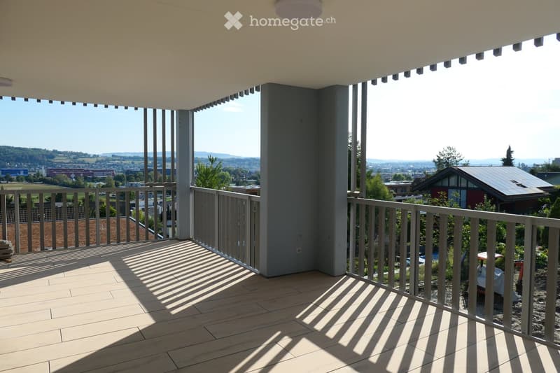 Balcony with wooden flooring, metal railing, and a scenic view of a city and surrounding landscape.
