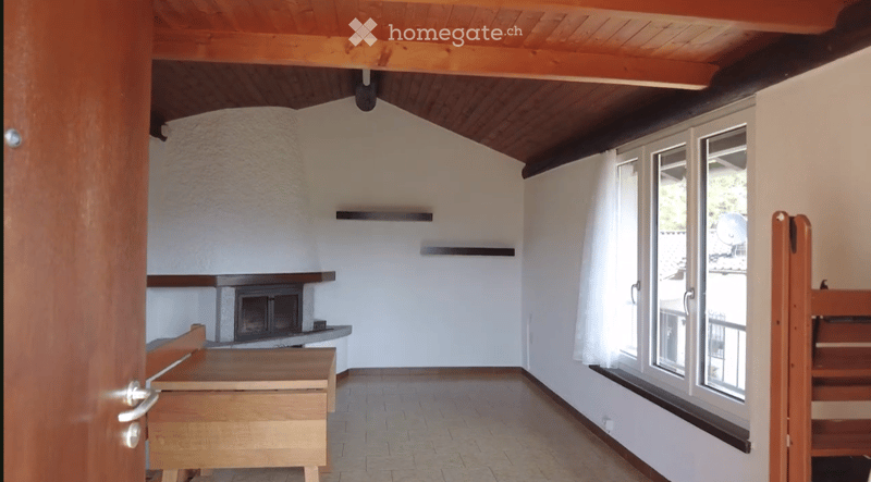 Empty room with a fireplace, wooden ceiling, large windows, and a wooden bench near the door.