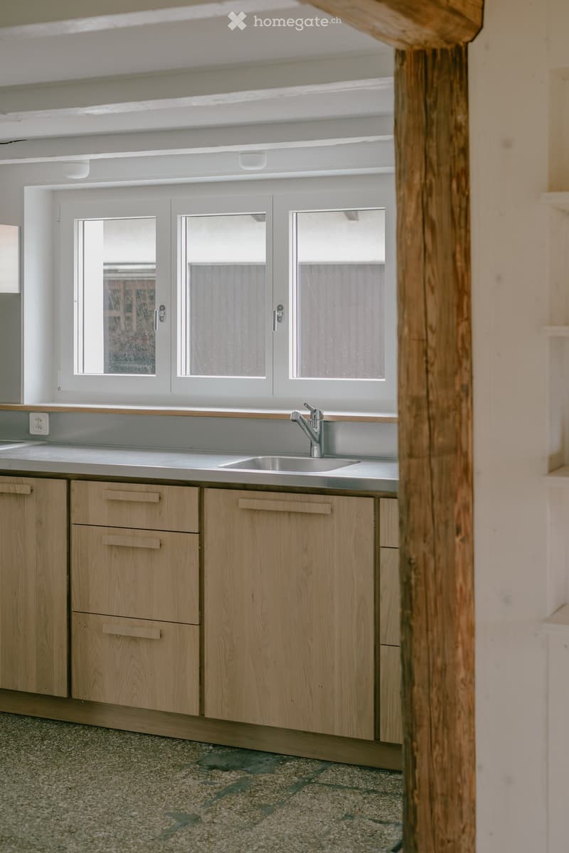 Modern kitchen with light wooden cabinets, a stainless steel sink, and a sleek faucet. The space features large windows with frosted glass panes, allowing natural light to fill the room.
