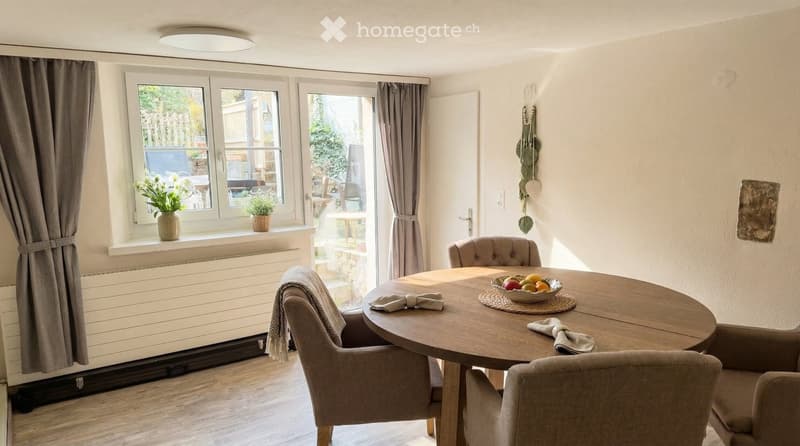 Dining room with wooden table, chairs, and a window with plants