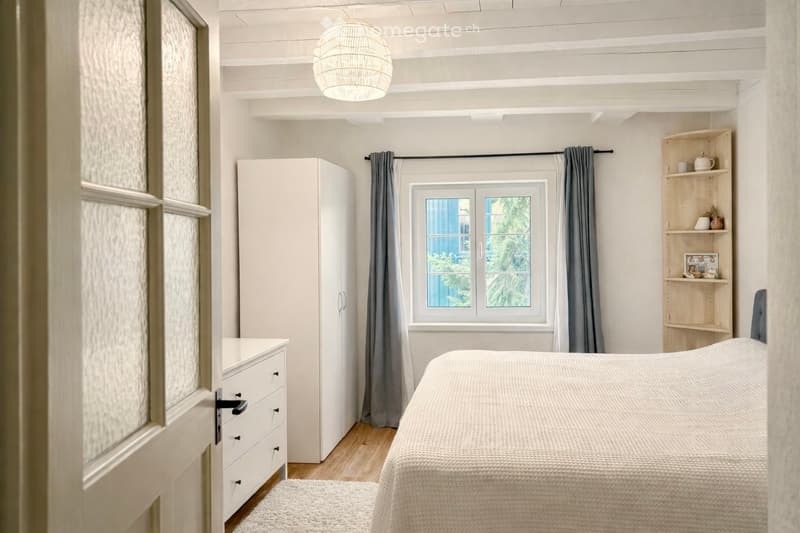 Bedroom with bed, white wardrobe, white drawers, white rug, white ceiling, white walls, window with curtains, wooden floor, lamp