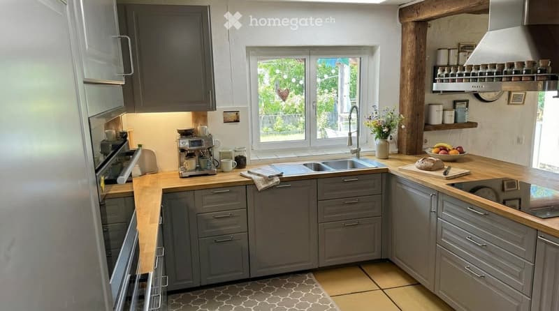 modern kitchen with wooden countertops, stainless steel sink, gas stove, refrigerator, gray cabinets, window with view to the outside, wooden beams