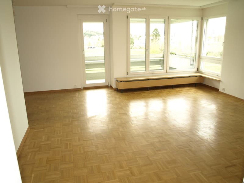 Empty room with wooden herringbone flooring, large windows, and a radiator cover. No furniture or equipment present.