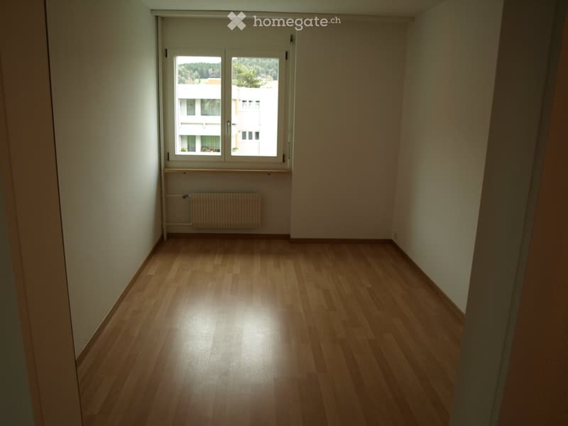 Empty room with wooden flooring, white walls, and a window with a radiator below it.