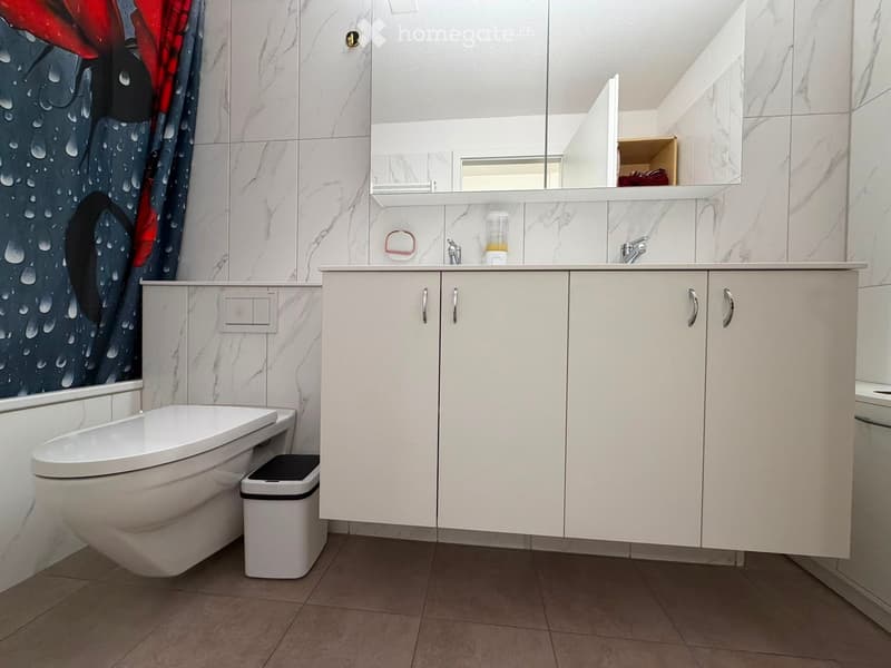 Modern bathroom with white cabinets, a toilet, a mirror, and a decorative shower curtain featuring a water droplet design.