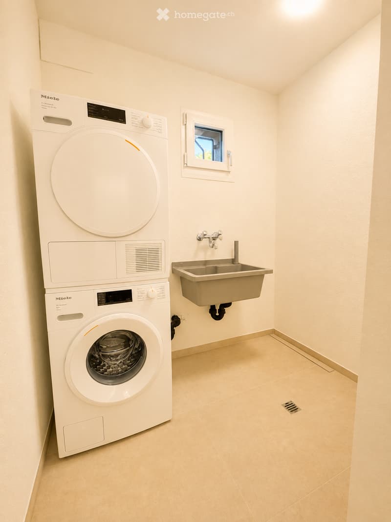 Clean, modern bathroom with a white washing machine, a stainless steel sink, and a small window.