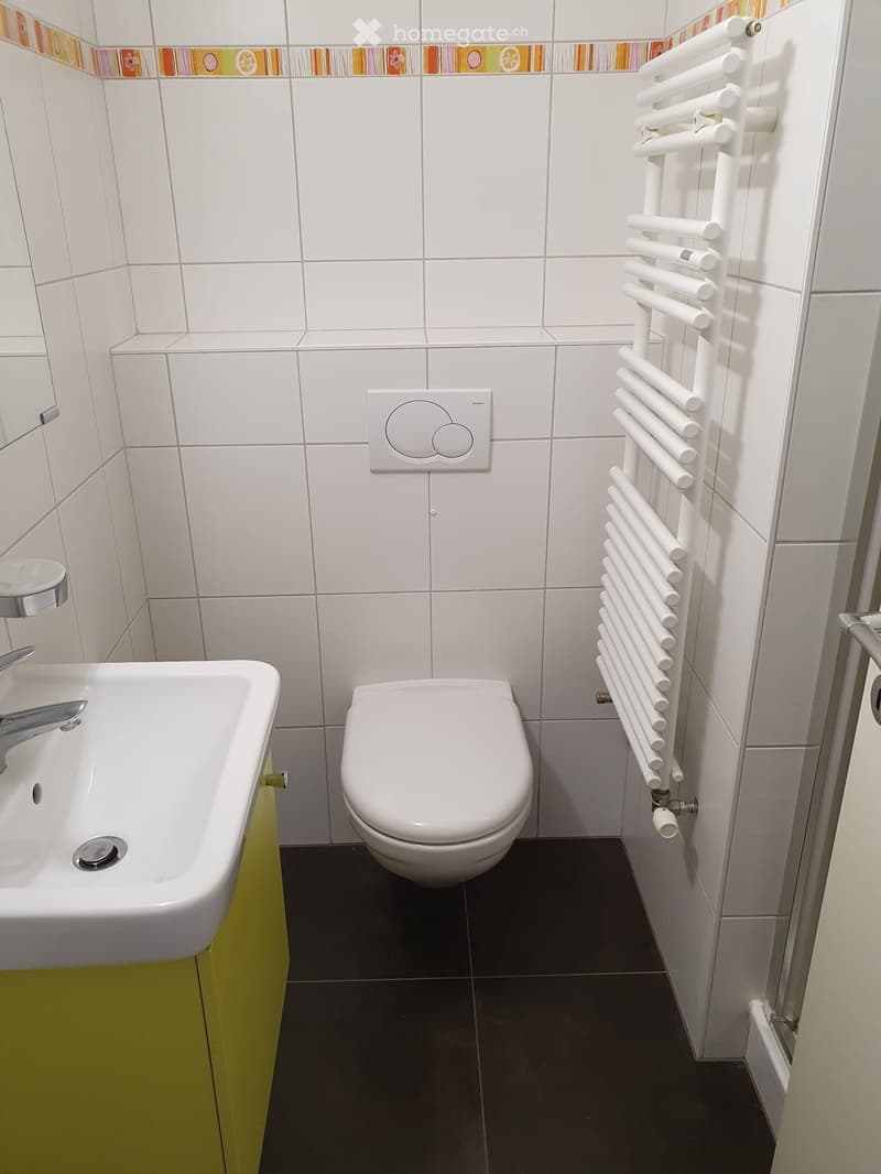 Modern bathroom with white tiles, a sink with a chrome faucet, a toilet, a white radiator, and a decorative border above the tiles.