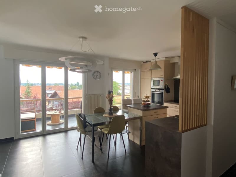 Open-plan kitchen and dining area with modern furniture, large sliding glass doors leading to a balcony, and a view of the neighborhood.