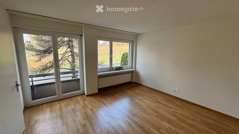Empty room with wooden flooring, large sliding glass door leading to a balcony, and a window with a radiator below it.