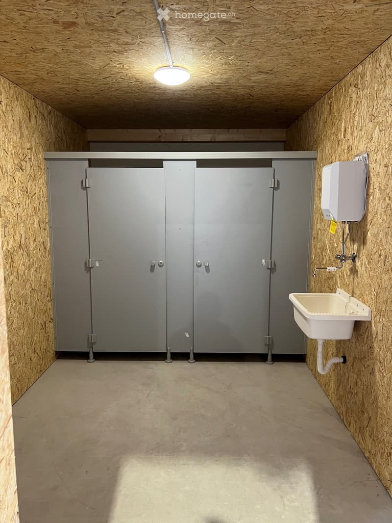 Empty bathroom with wooden walls and ceiling, two stall doors, a sink with a faucet, and a hand dryer on the wall.