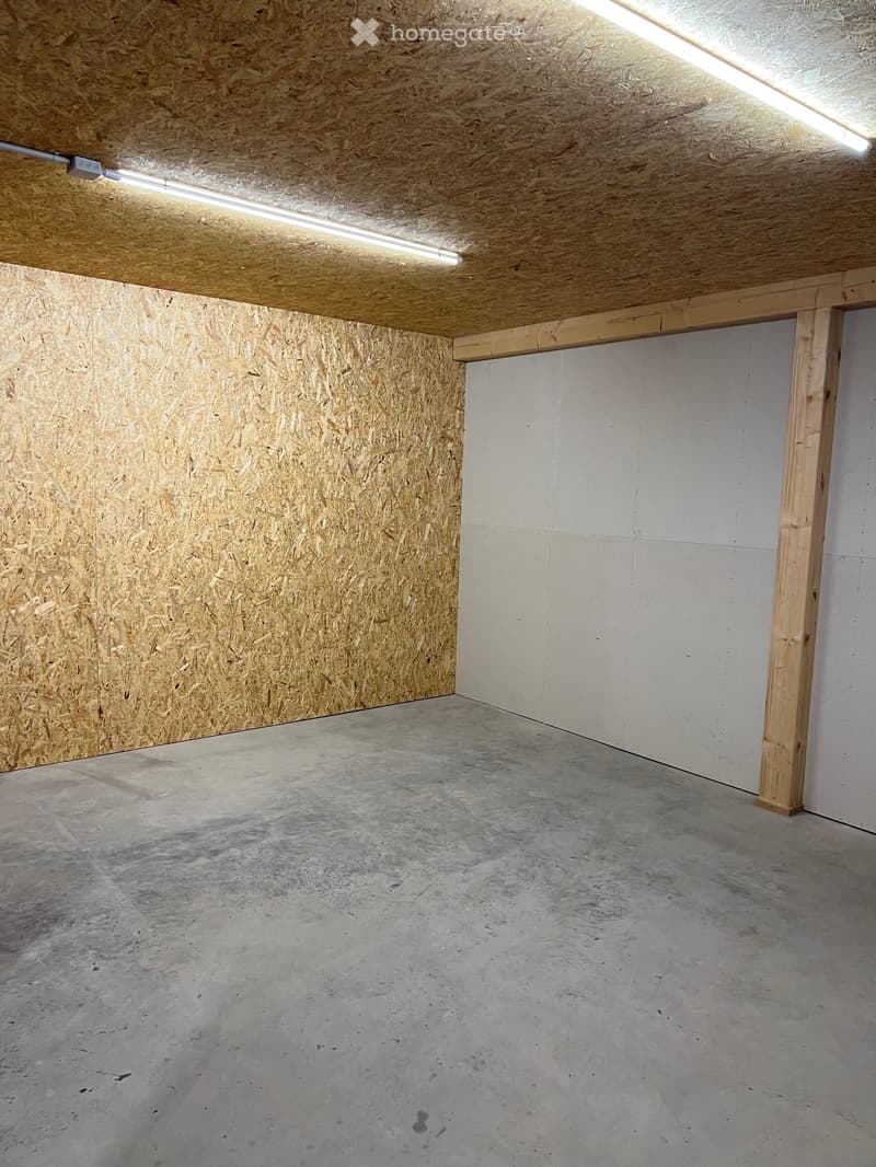 Empty garage with concrete floor, wooden ceiling, and exposed wooden beams. No furniture or equipment present.