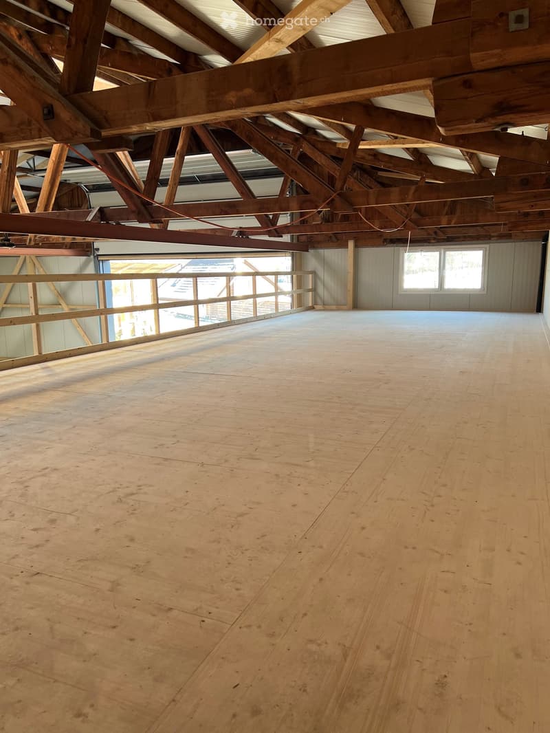 Empty room with wooden floor and exposed wooden beams on the ceiling. Natural light comes through windows on one side.