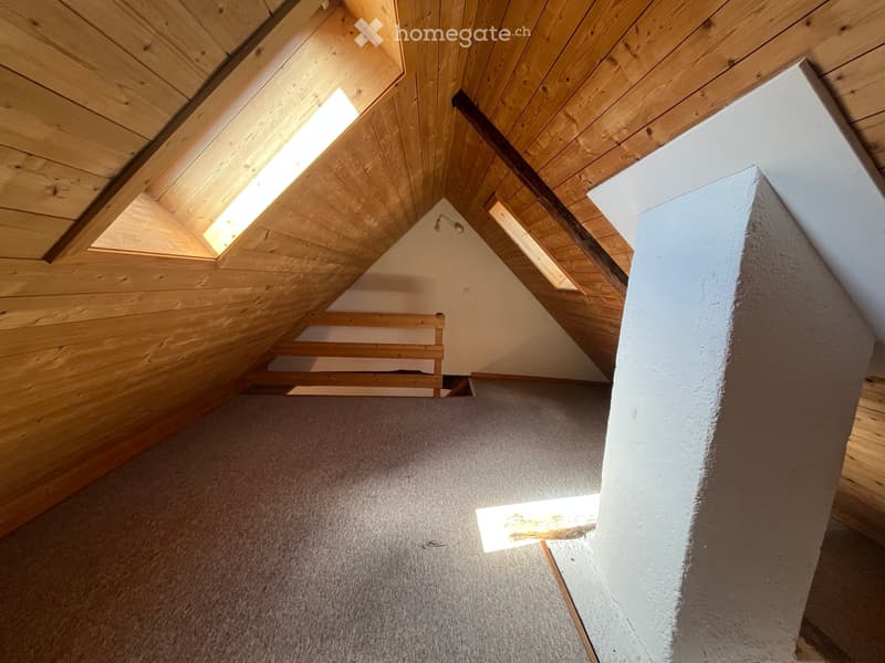 Empty attic space with wooden slanted ceilings, skylights, and a small bench against the wall.