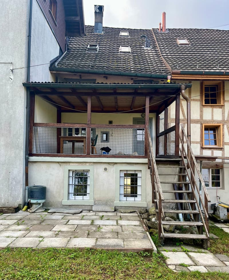 Two-story house with a tiled roof, wooden balcony, and stone steps leading to the entrance.