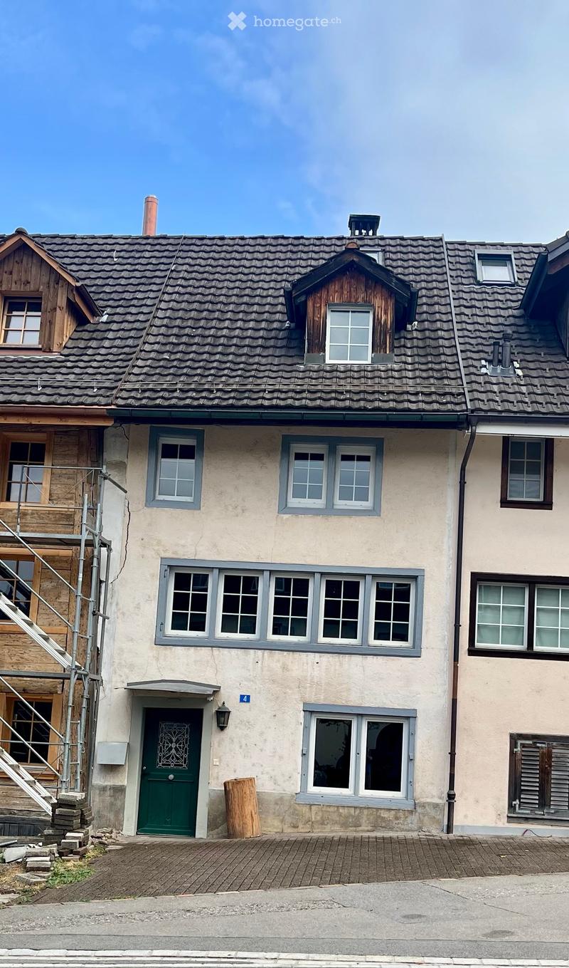 Two-story house with a tiled roof, multiple windows, green front door, and a wooden staircase leading to the entrance.