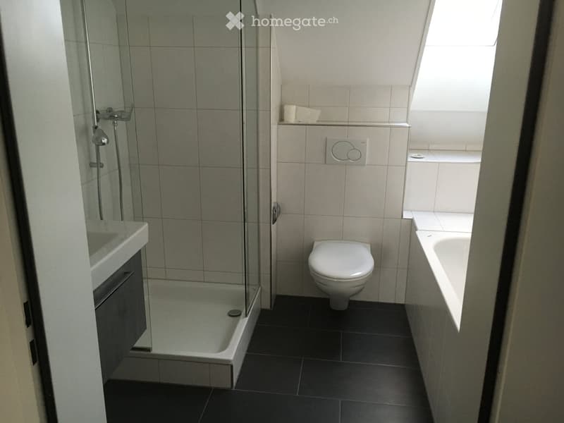 Modern bathroom with a toilet, bathtub, shower, and sink. The shower has a glass enclosure, and the floor is tiled in dark gray.