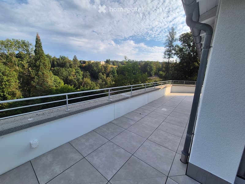 Balcony with tiled floor, white railing, and a view of trees and a hillside.