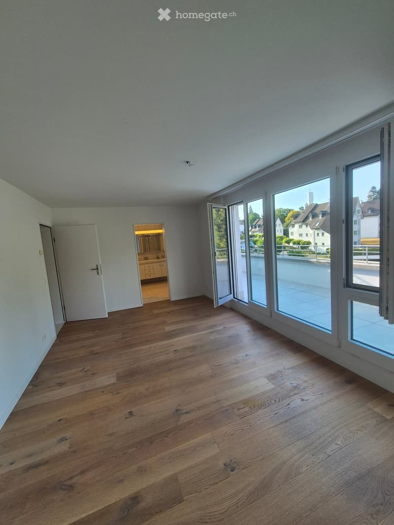 Empty room with wooden flooring, large glass sliding doors leading to a balcony, and a visible bathroom area through an open doorway.
