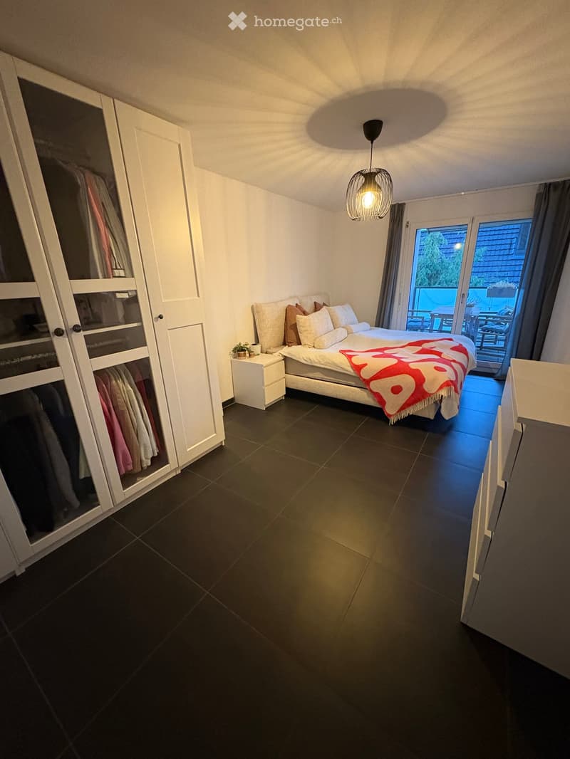 Modern bedroom with a large bed, nightstand, wardrobe, and a view to a balcony or terrace area.