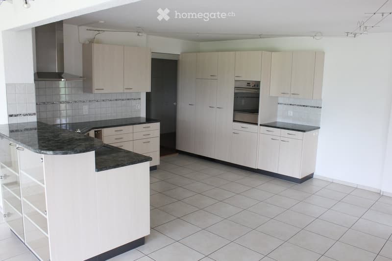 Modern kitchen with white cabinets, granite countertop, built-in oven, and range hood. The space features tiled flooring and a central island with storage drawers.