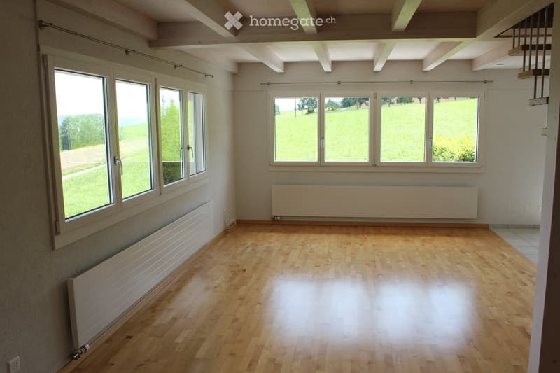 Empty room with wooden flooring, large windows, radiators, and exposed wooden beams on the ceiling.