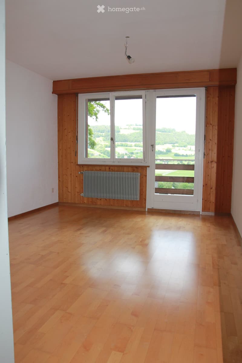 Empty room with wooden flooring, white walls, large windows, and a radiator. No furniture or equipment present.