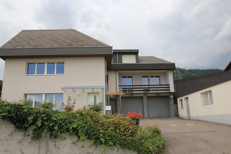 Two-story house with beige exterior, large windows, garage, and balcony on the upper level.