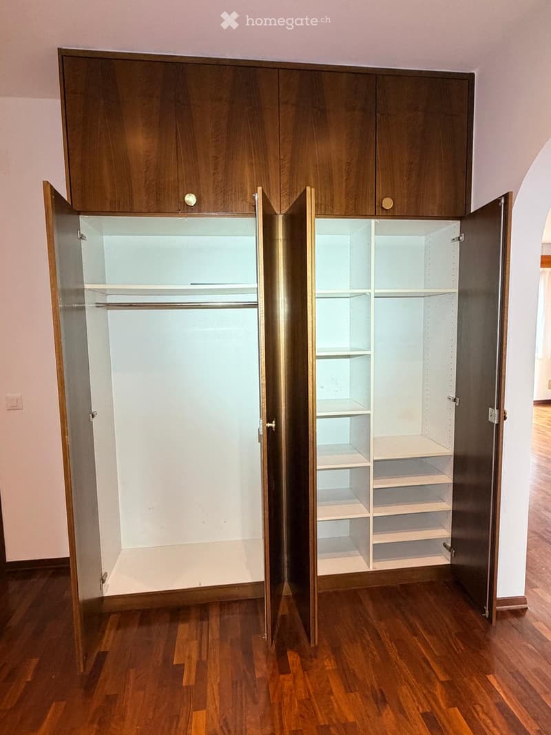 Empty room with wooden floor and large, open wooden closet with multiple shelves and hanging space.