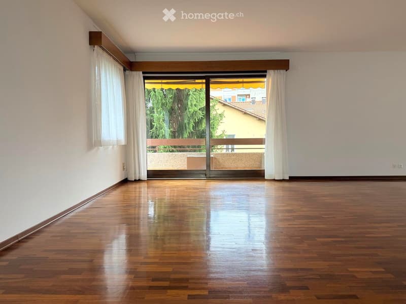 Empty room with wooden flooring, large sliding glass doors leading to a balcony, and white walls.