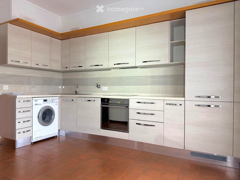 Modern kitchen with light-colored cabinets, stainless steel appliances, and a tiled floor.