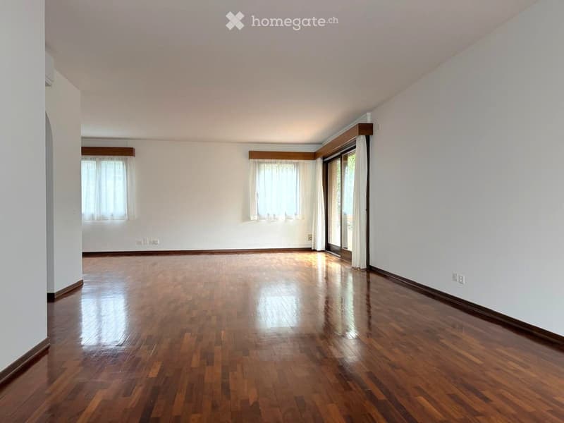 Empty room with wooden flooring, white walls, and large windows with curtains. No furniture or equipment present.