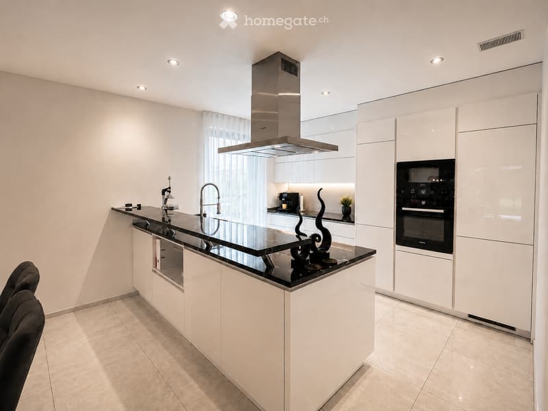 Modern kitchen with white cabinets, black countertop, island, sink, faucet, oven, range hood, and decorative sculpture.