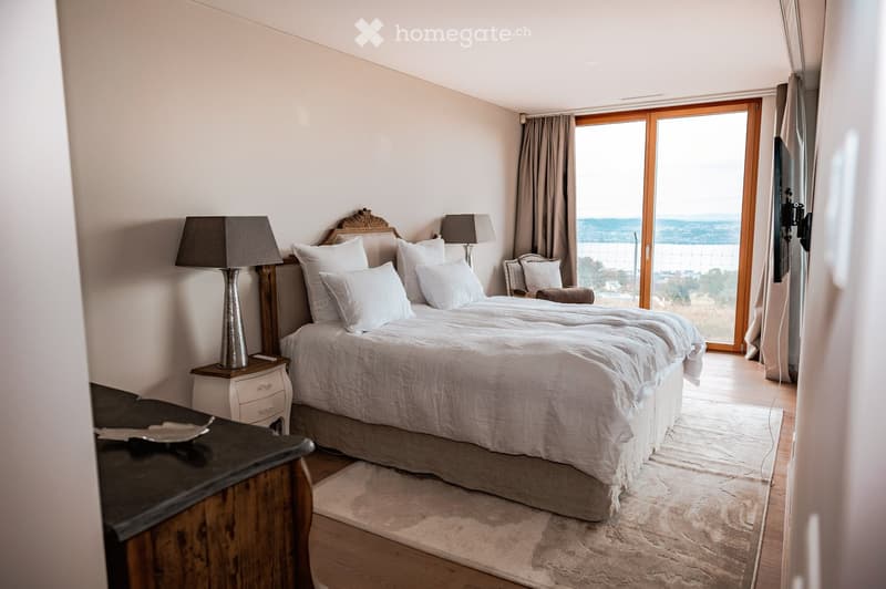 Elegant bedroom with a large bed, nightstands, lamps, a chair, and a scenic view through large windows.