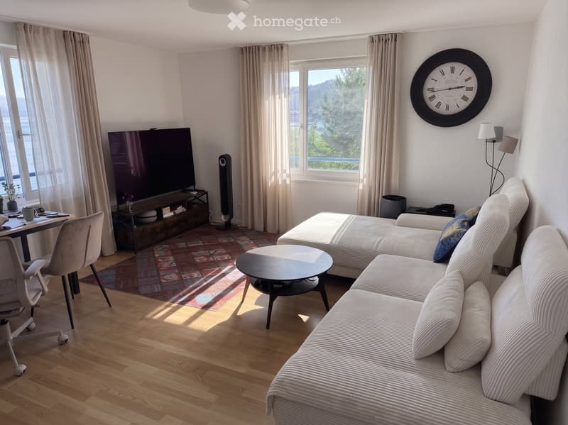 Modern living room with a sectional sofa, coffee table, TV, and large windows with curtains.