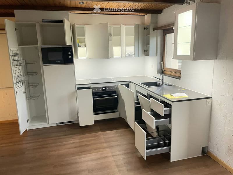 Modern kitchen with white cabinets, stainless steel appliances, and wooden flooring.