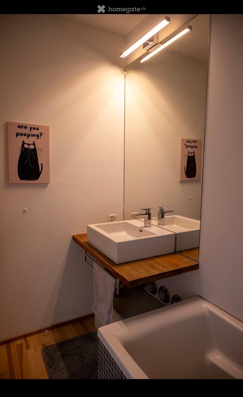 Modern bathroom with double sink, wooden countertop, mirror, bathtub, and decorative artwork.