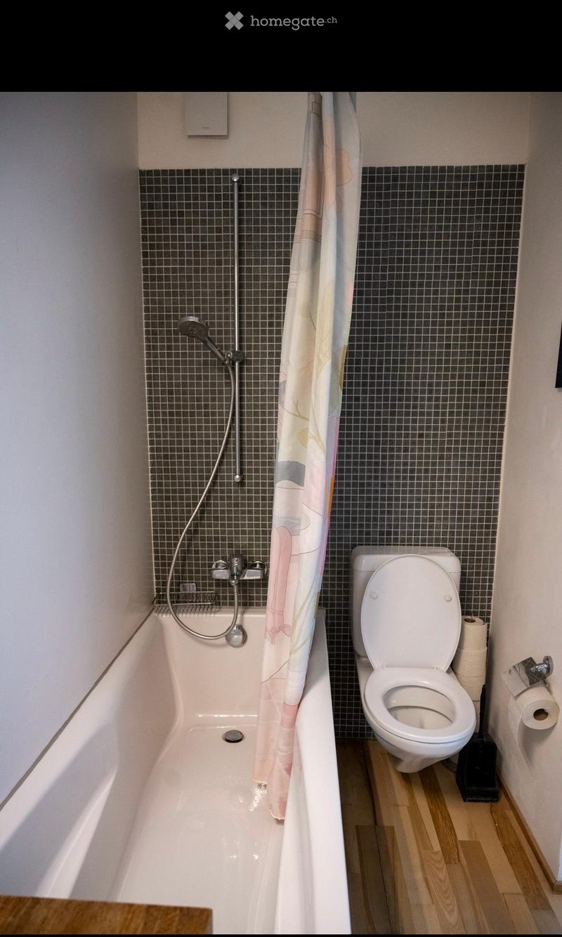 Bathroom with a bathtub, toilet, shower curtain, and a wooden floor.