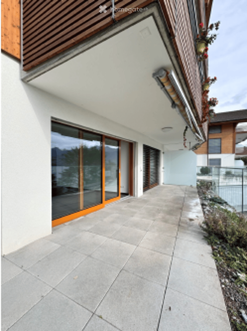 Balcony / Terrace. Balcony with large sliding glass doors, concrete floor, wooden railing, and a view of the surrounding area.