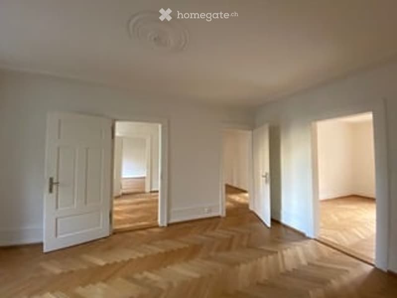 Empty room with wooden flooring and white walls, featuring multiple doors and a ceiling light fixture.