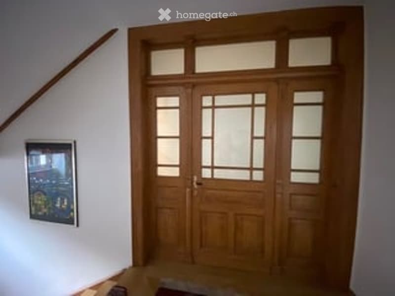 A hallway with a wooden double door featuring glass panels, a staircase to the left, and a framed picture on the wall.