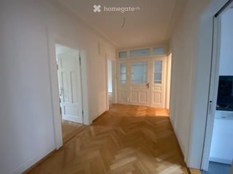 Empty hallway with wooden flooring, white walls, and doors leading to other rooms.