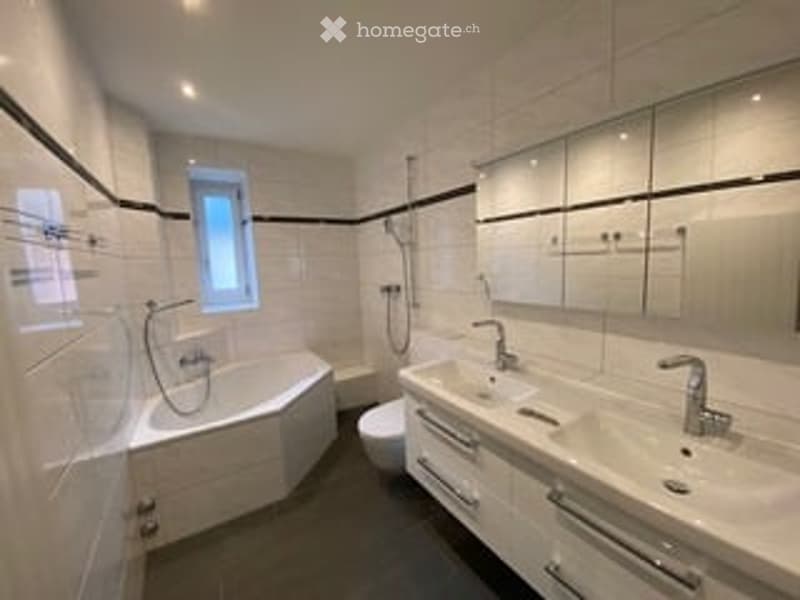 Modern bathroom with white tiles, a bathtub, a sink with a mirror, and a toilet.