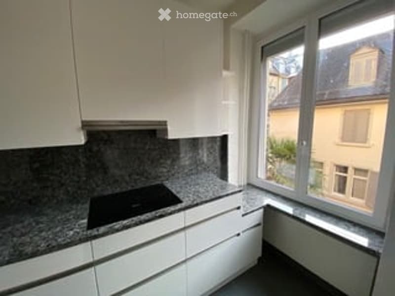 Modern kitchen with white cabinets, granite countertop, and a built-in stove. Large window offers a view of the street.