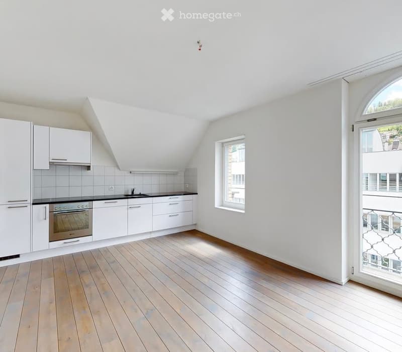 Bright, modern kitchen with white cabinets, stainless steel oven, and wooden flooring. Features a large window and a door leading to a balcony.