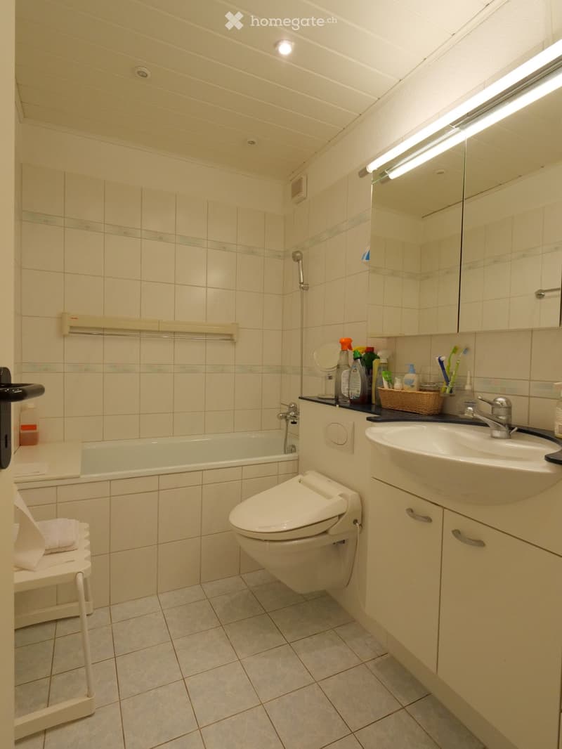 Clean, modern bathroom with a bathtub, toilet, sink, mirror, and various toiletries neatly arranged on the counter.