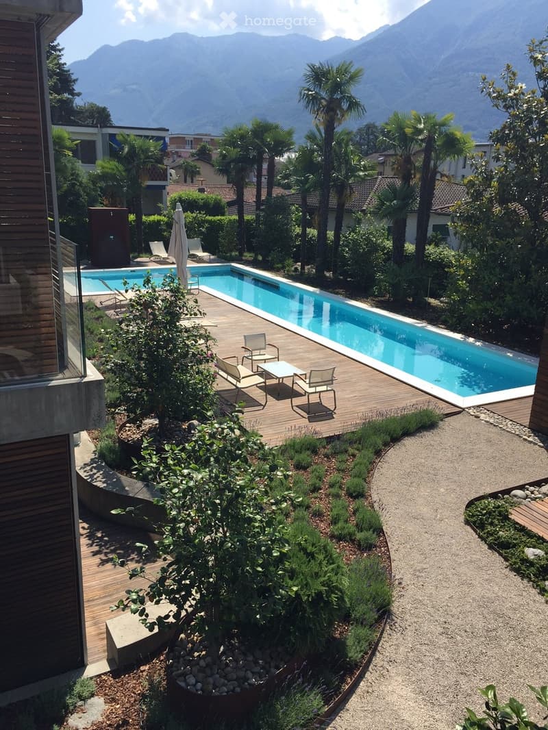 Outdoor garden area with a swimming pool, wooden decking, lounge chairs, and surrounding greenery with a scenic mountain view in the background.