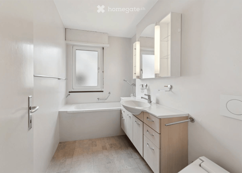Modern bathroom with a bathtub, sink, mirror, and wooden cabinet. Features a window with frosted glass and a door with a silver handle.